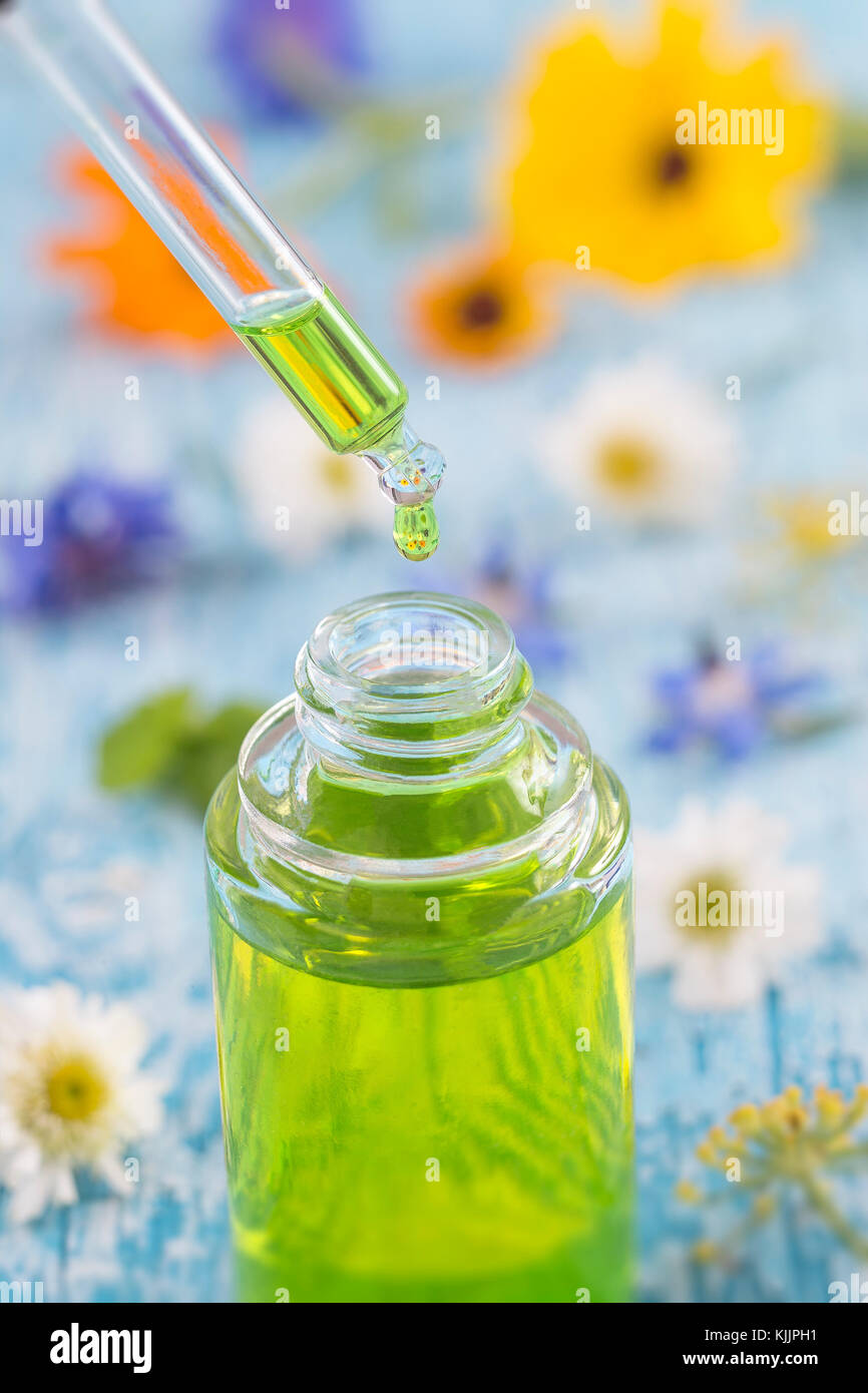 Trasparente bottiglie in vetro con gocce di liquido essenziale in contagocce su sfondo di legno con fiori di medicinali Foto Stock