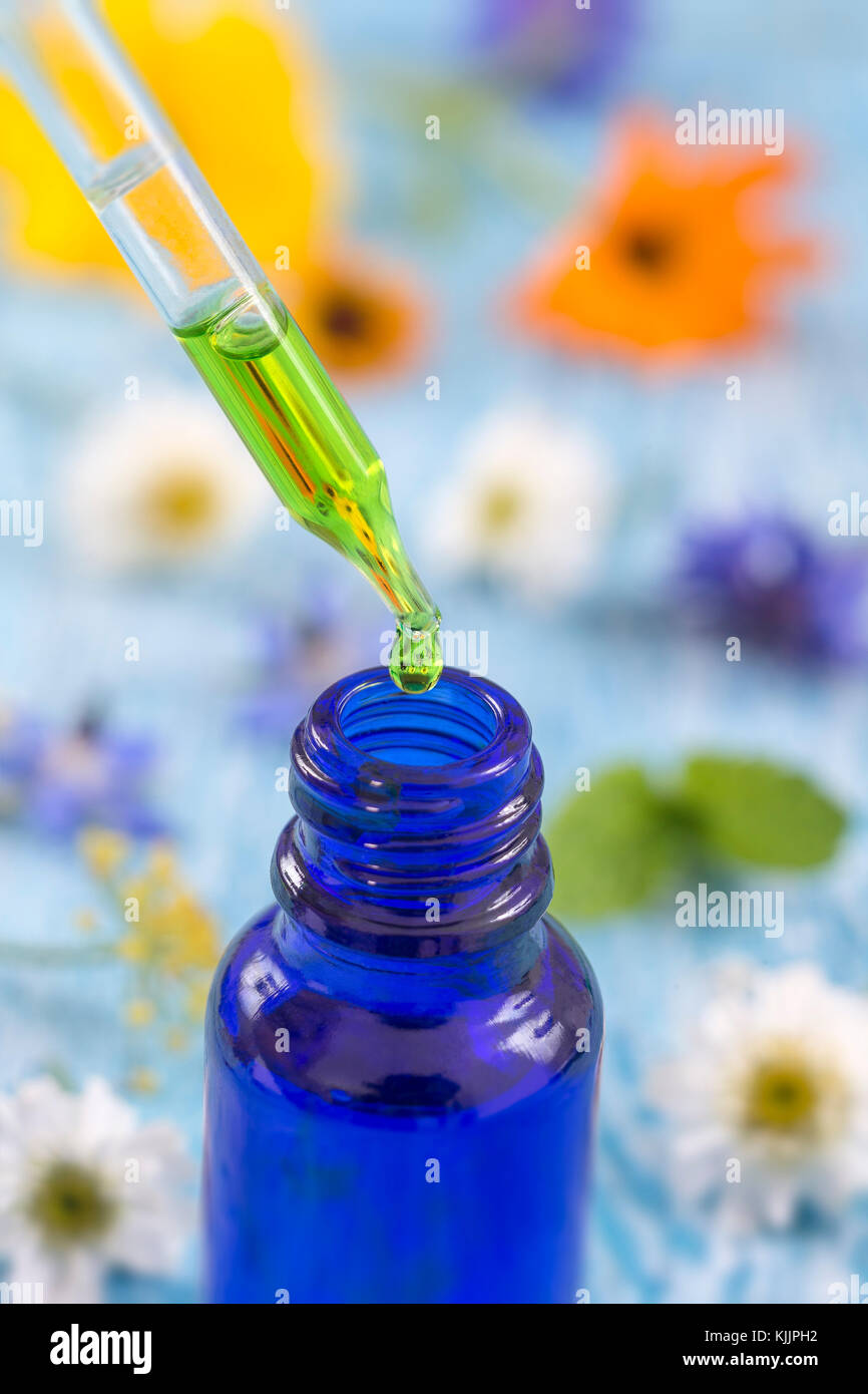 Trasparente bottiglie in vetro con gocce di liquido essenziale in contagocce su sfondo di legno con fiori di medicinali Foto Stock
