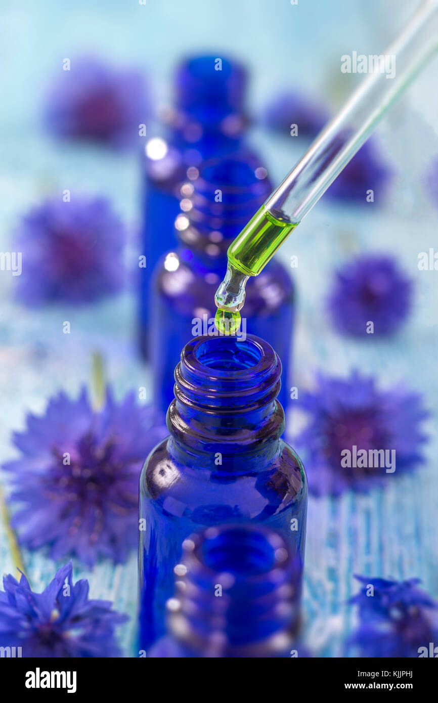 Trasparente bottiglie in vetro con gocce di liquido essenziale in contagocce su sfondo di legno con fiori di medicinali Foto Stock