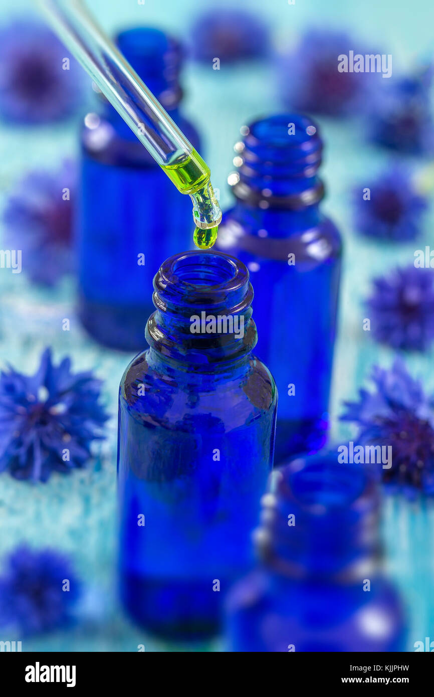 Trasparente bottiglie in vetro con gocce di liquido essenziale in contagocce su sfondo di legno con fiori di medicinali Foto Stock