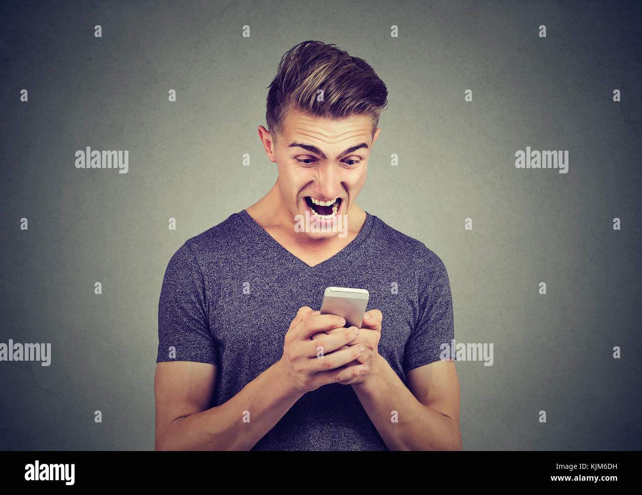 Frustrati angry man la lettura di un messaggio di testo sullo smartphone urlando isolato su sfondo grigio Foto Stock