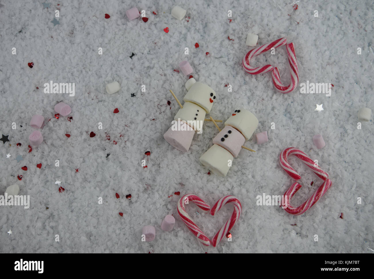 Romantico Inverno immagine fotografia di marshmallows a forma di pupazzo di neve con iced su sorrisi e giacente nella neve con cuori rossi stelle e candy canes Foto Stock