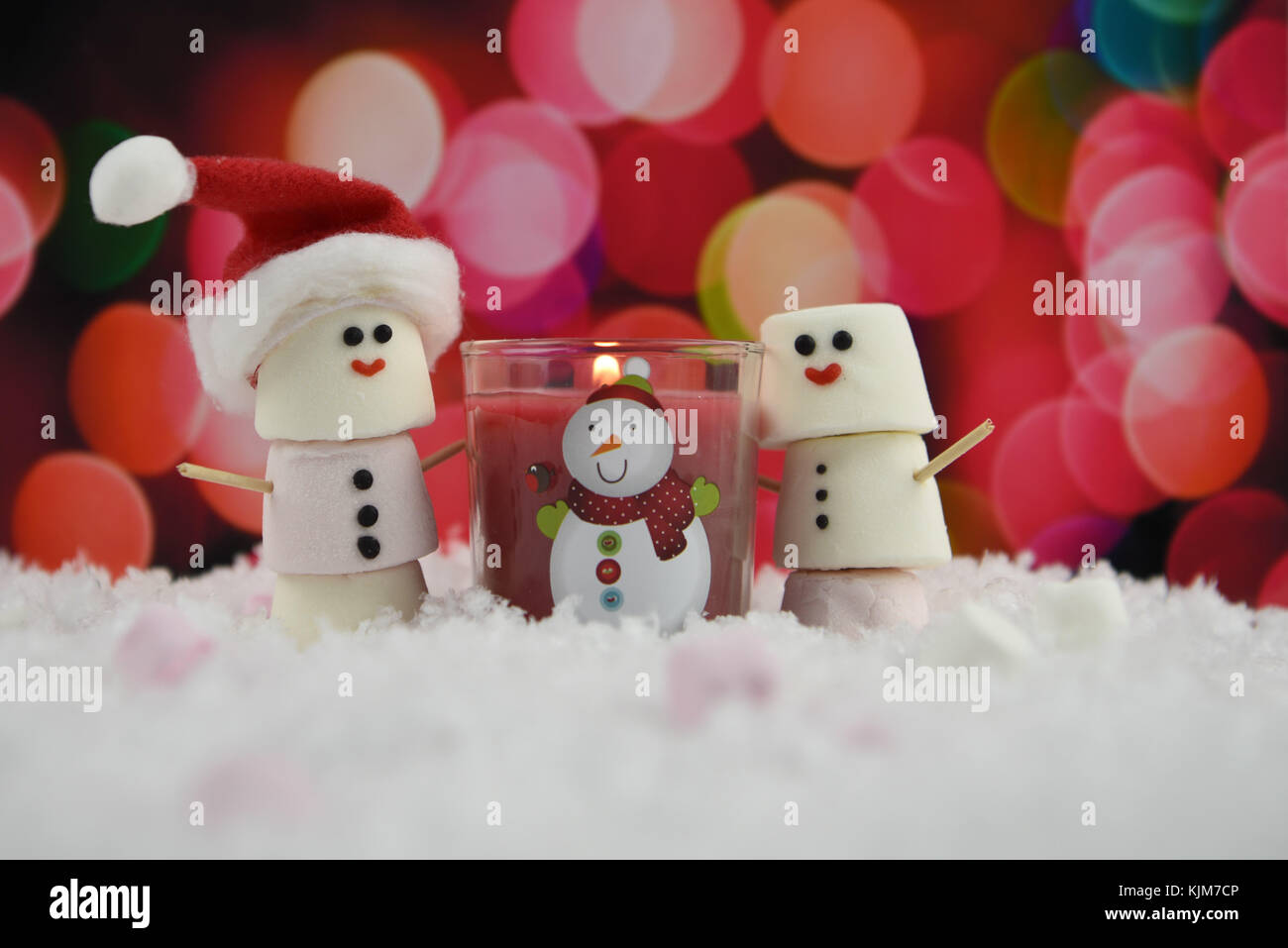 Caldo Inverno stagione di natale immagine di fotografia con rosso illuminato candela e marshmallows a forma di pupazzo di neve con iced sul sorriso e in piedi nella neve Foto Stock