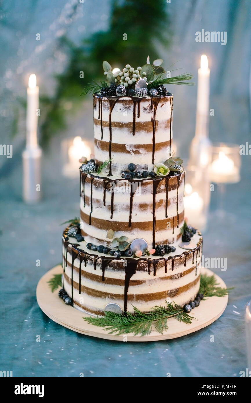 La cottura, dolcezza, il concetto di matrimonio. close up di tre tier incredibile torta con bianco e marrone e streeps glassa di cioccolato sui bordi e decorata con fiori Foto Stock