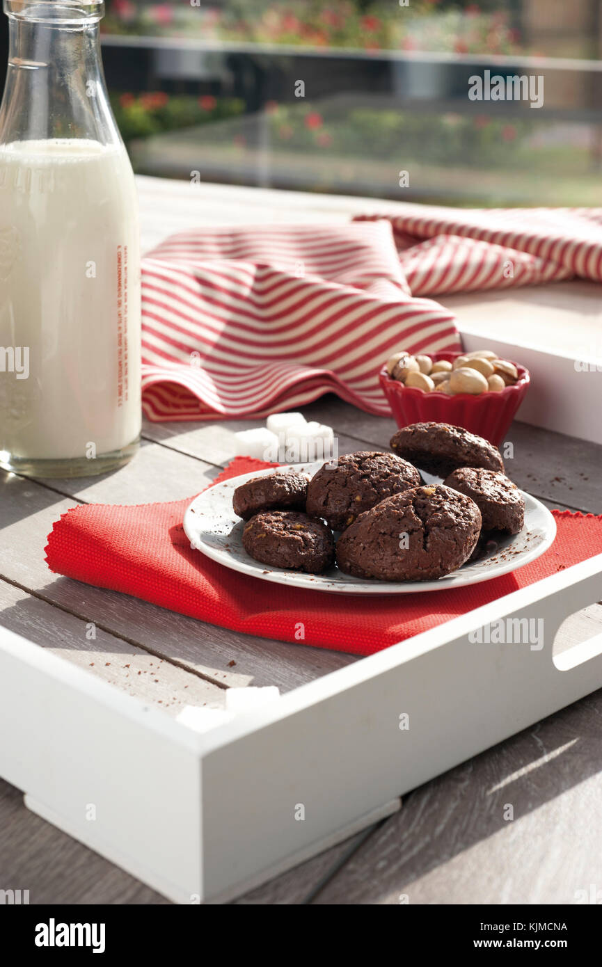 Rustico cacao Biscotti e pistacchi sul vassoio in legno con una bottiglia di latte, zuccheriera alluminio, pistacchi freschi, cubetti di zucchero e tovaglia con striping Foto Stock