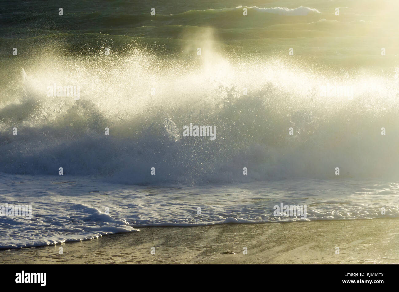 Una tempesta in onda sulla riva con la schiuma e un sacco di spruzzo su una spiaggia di sabbia sotto la luce diretta del sole Foto Stock