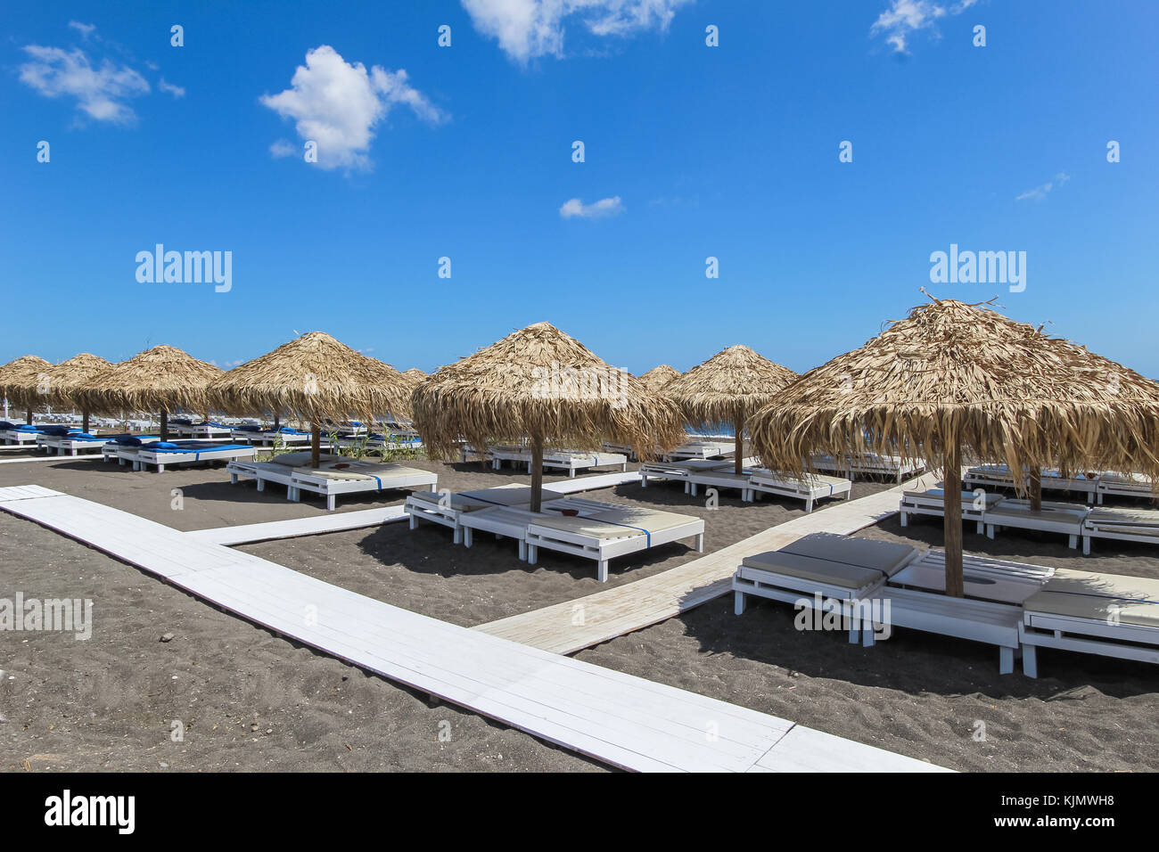 Una fila di sdraio e ombrelloni in spiaggia sulla spiaggia di sabbia nera, Santorini Island, Grecia Foto Stock