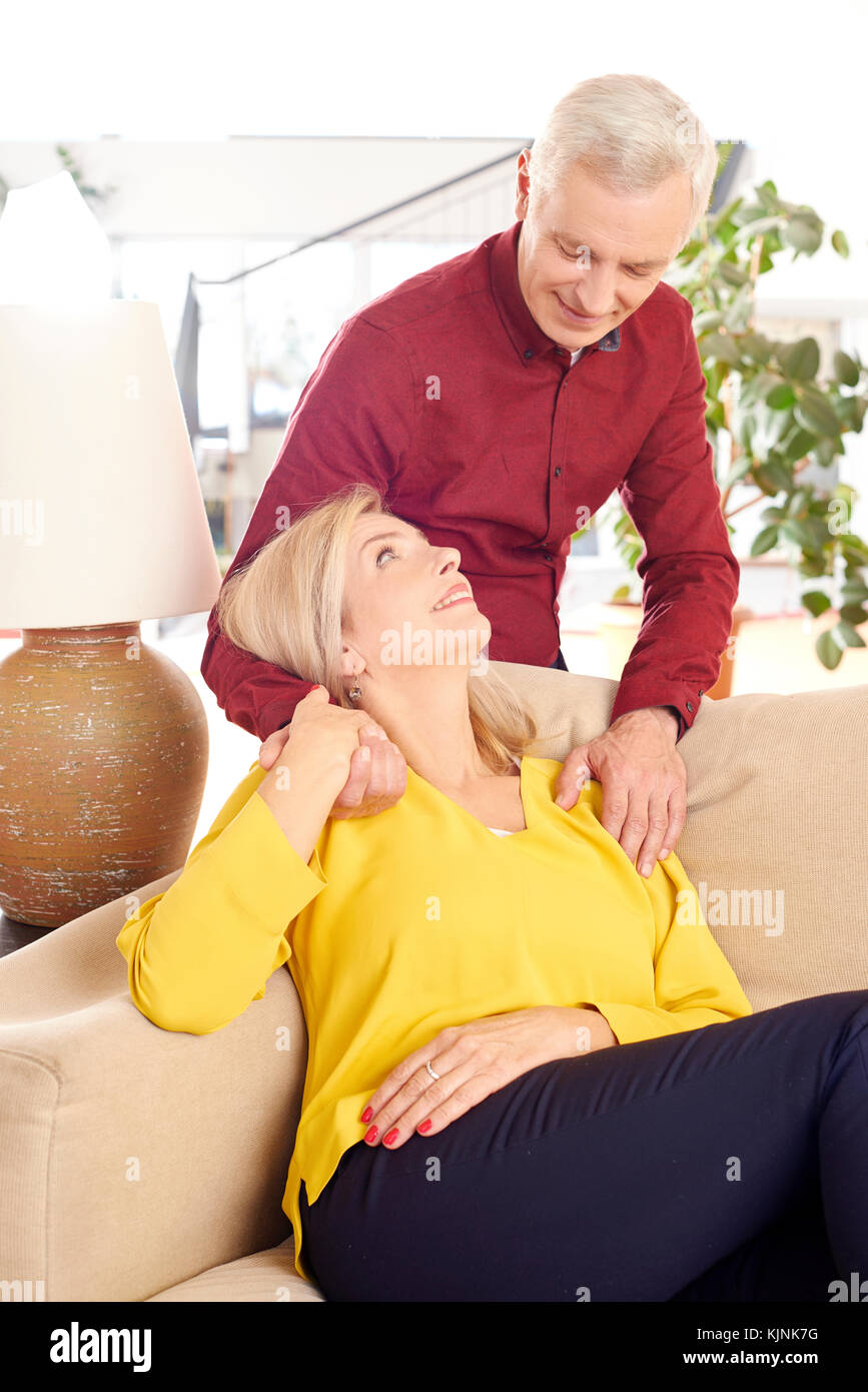 Inquadratura di un felice senior in un momento di relax a casa. bella donna matura seduti sul divano mentre suo marito costeggiata da dietro mentre in salotto. Foto Stock