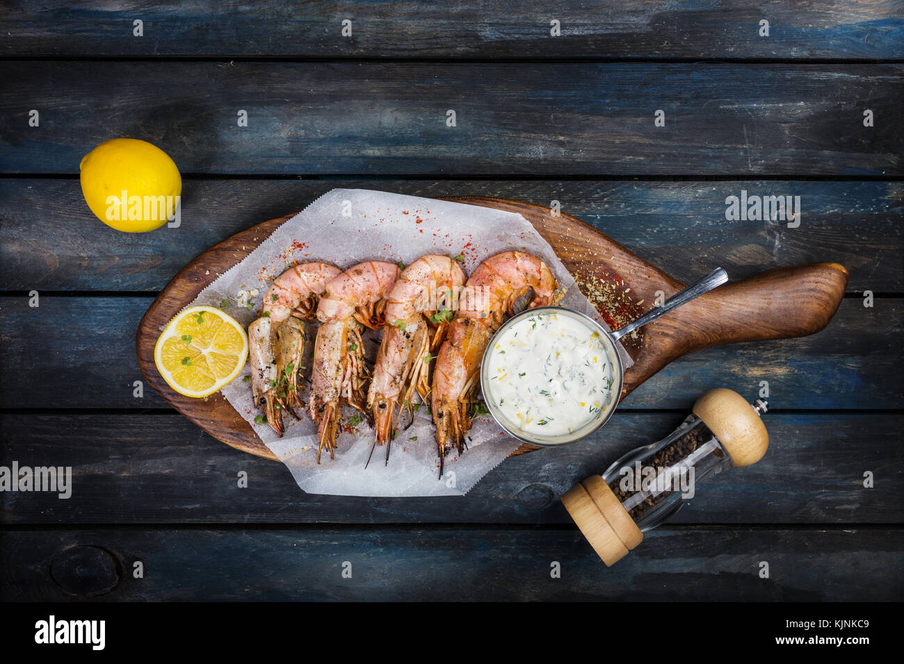 Deliziosi gamberi argentina o langoustine con sugo bianco pepe-pot e la metà di un limone su una tavola di legno. vista superiore Foto Stock