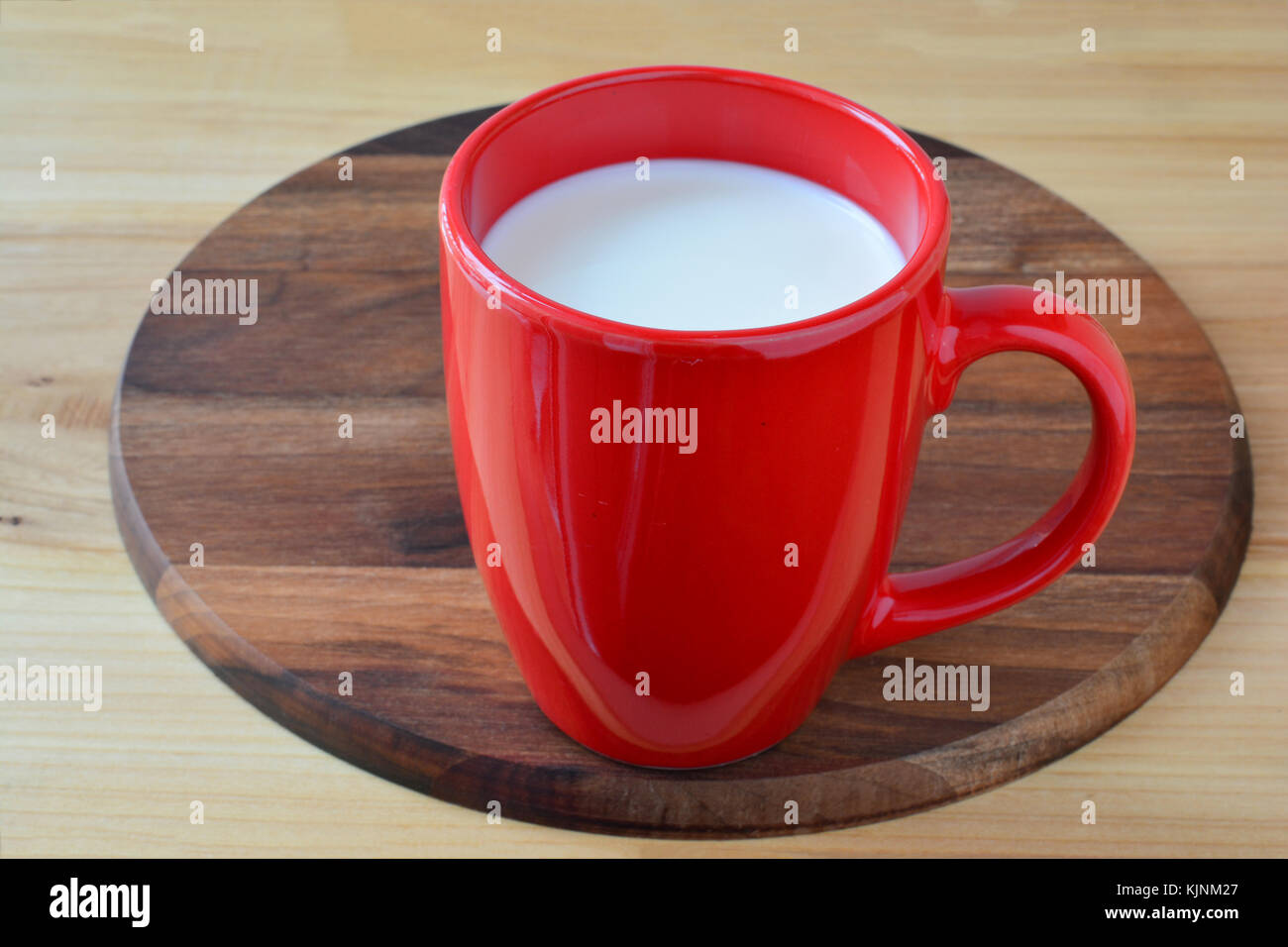 Il latte fresco in big red cup on dark nutwood platter Foto Stock