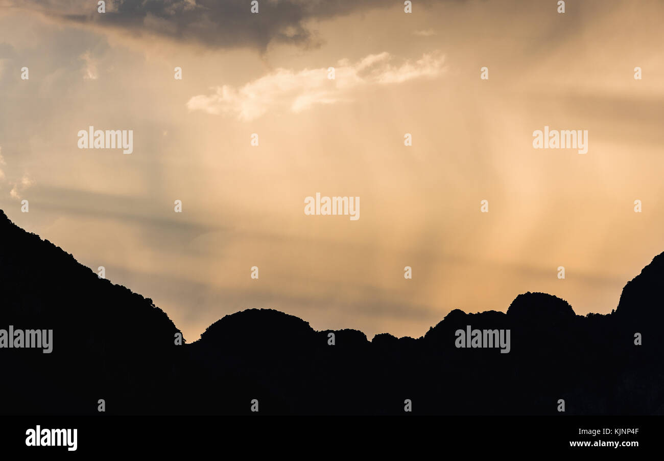 La luce del sole del mattino cielo toccando la pioggia soffiando dal vento sulla scena scura di profilarsi la gamma della montagna di Samet Nangshe, Phang Nga, Thailandia. Foto Stock