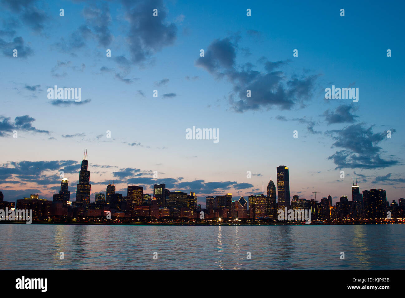 Lo skyline di Chicago brilla di notte, con grattacieli illuminati che si riflettono sul lago Michigan, mettendo in risalto l'iconica architettura urbana della città. Foto Stock