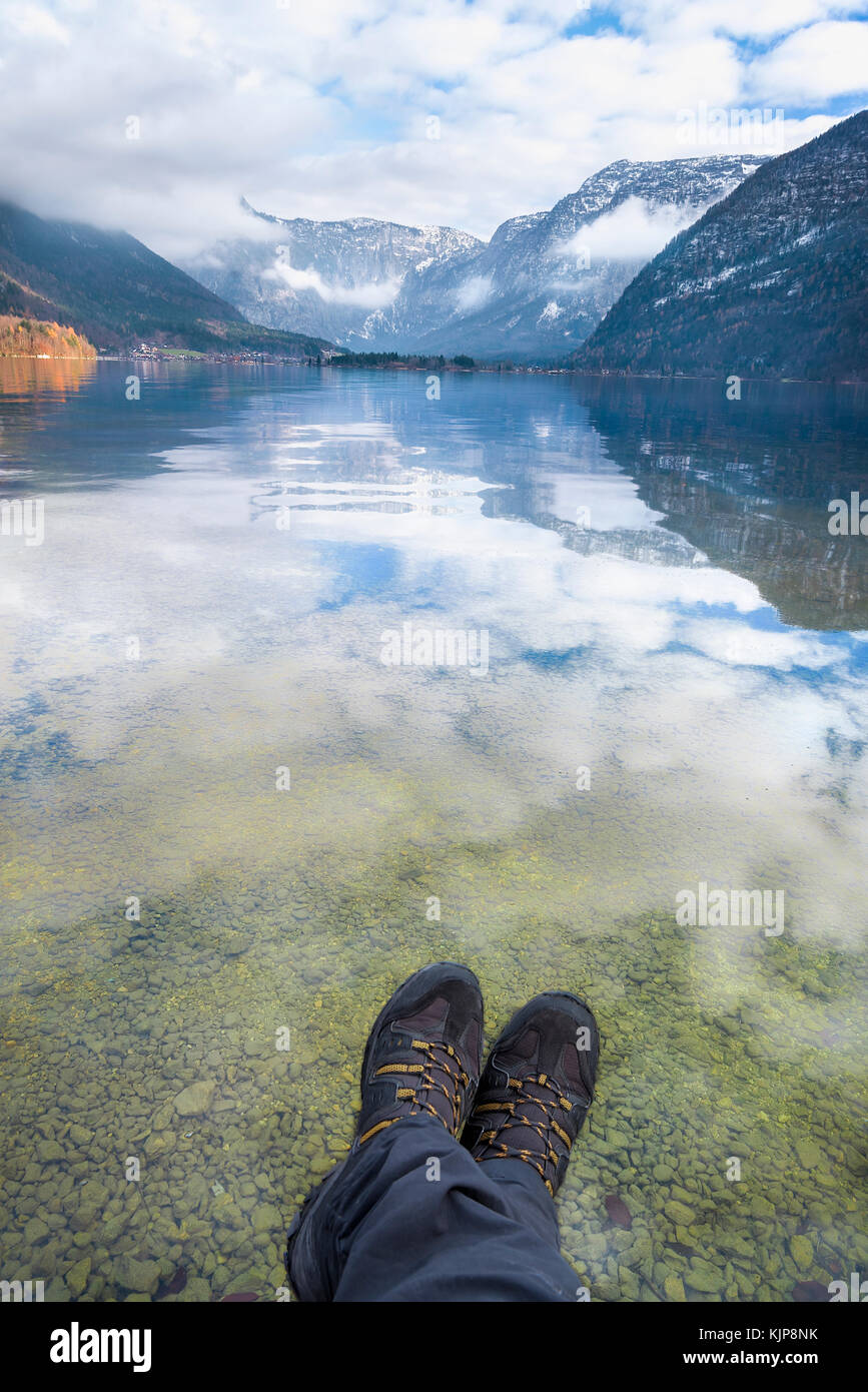 Escursioni a tema con immagine di un uomo le gambe e le montagne del Dachstein e il loro riflesso nel lago hallstatter, in Austria Foto Stock