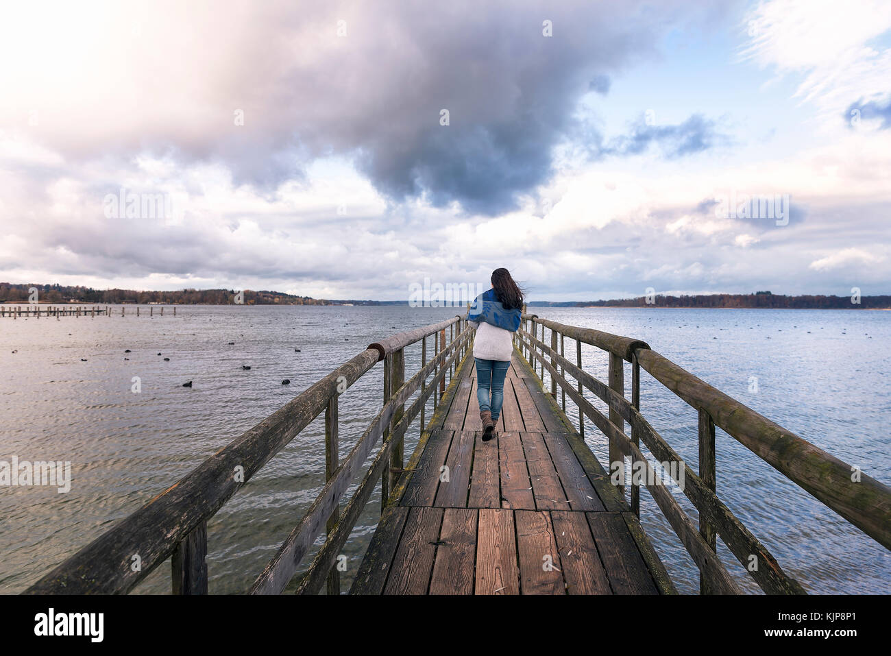 Giovane donna camminare da solo su un rustico ponte in legno sul lago Chiemsee, chiamato anche il mare bavarese, situato vicino a Rosenheim, Germania. Foto Stock