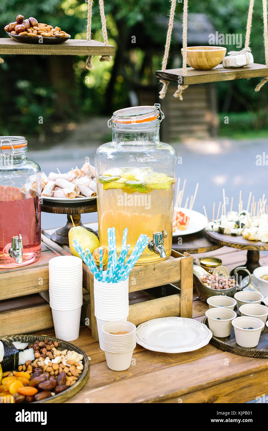 Pasto, estate, plesure concetto. Ci sono diversi tipi di succhi di frutta, frutta a guscio e frutta secca in bicchieri di carta e involtini primavera in vaso di legno sul tavolo Foto Stock