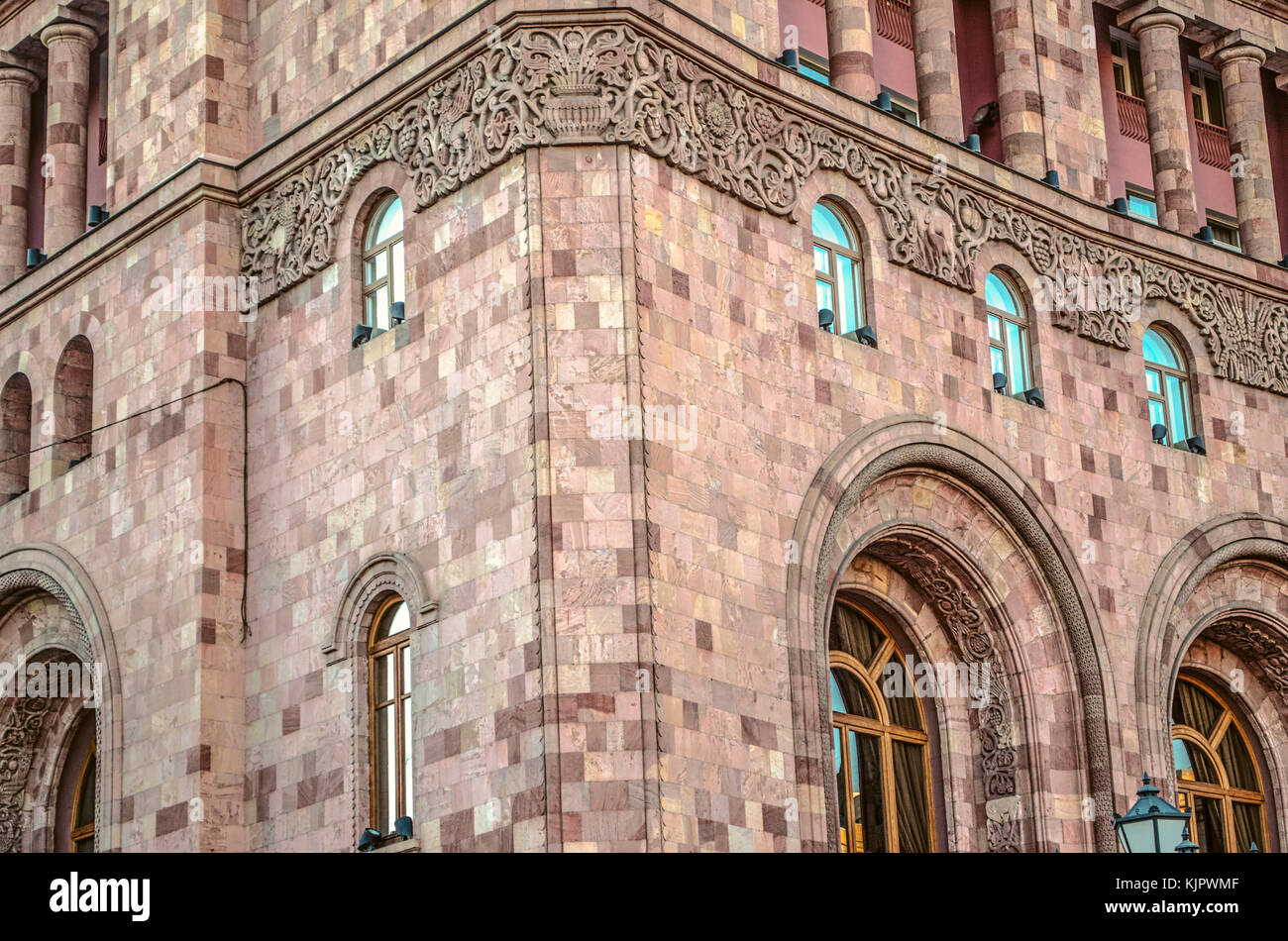 Bassorilievo con arredamento etnico su un edificio amministrativo di motley pietra sulla piazza centrale di Yerevan Foto Stock