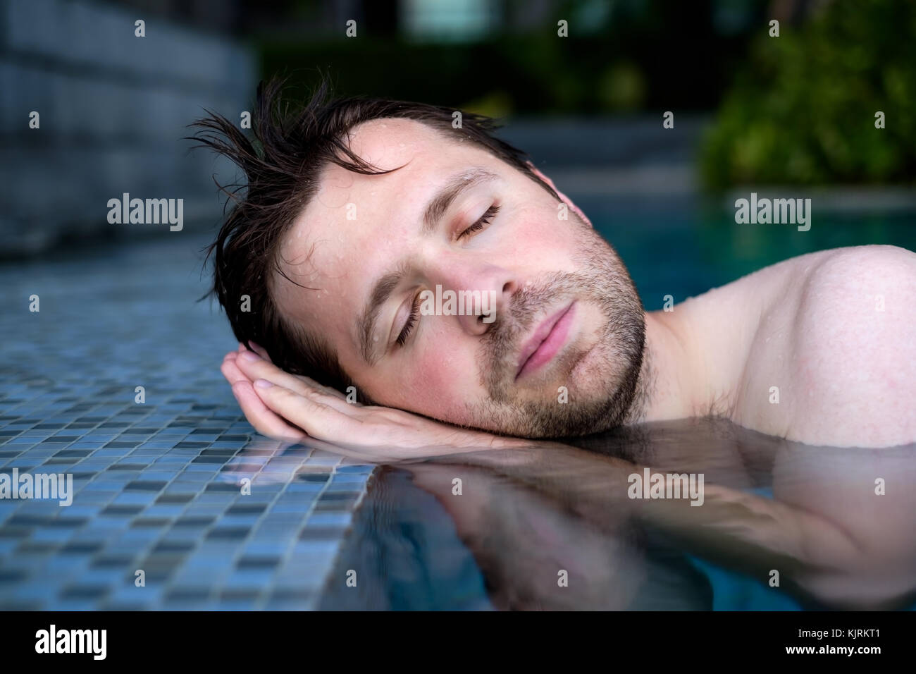 Un giovane uomo pretende che egli dorme sul bordo della piscina, mettendo le mani sotto la sua testa. Foto Stock