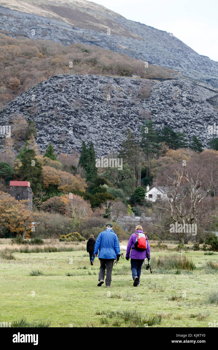 Escursionisti a piedi al di sotto di una collina di scorie di una cava di ardesia miniera o. Snowdonia, il Galles del Nord. Foto Stock