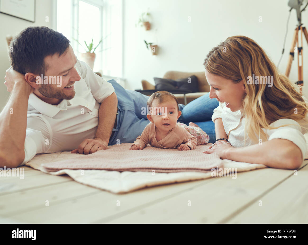 Sorridente coppia giovane giacente insieme su coperte sul loro soggiorno piano a casa con il loro adorabile figlia bambino Foto Stock