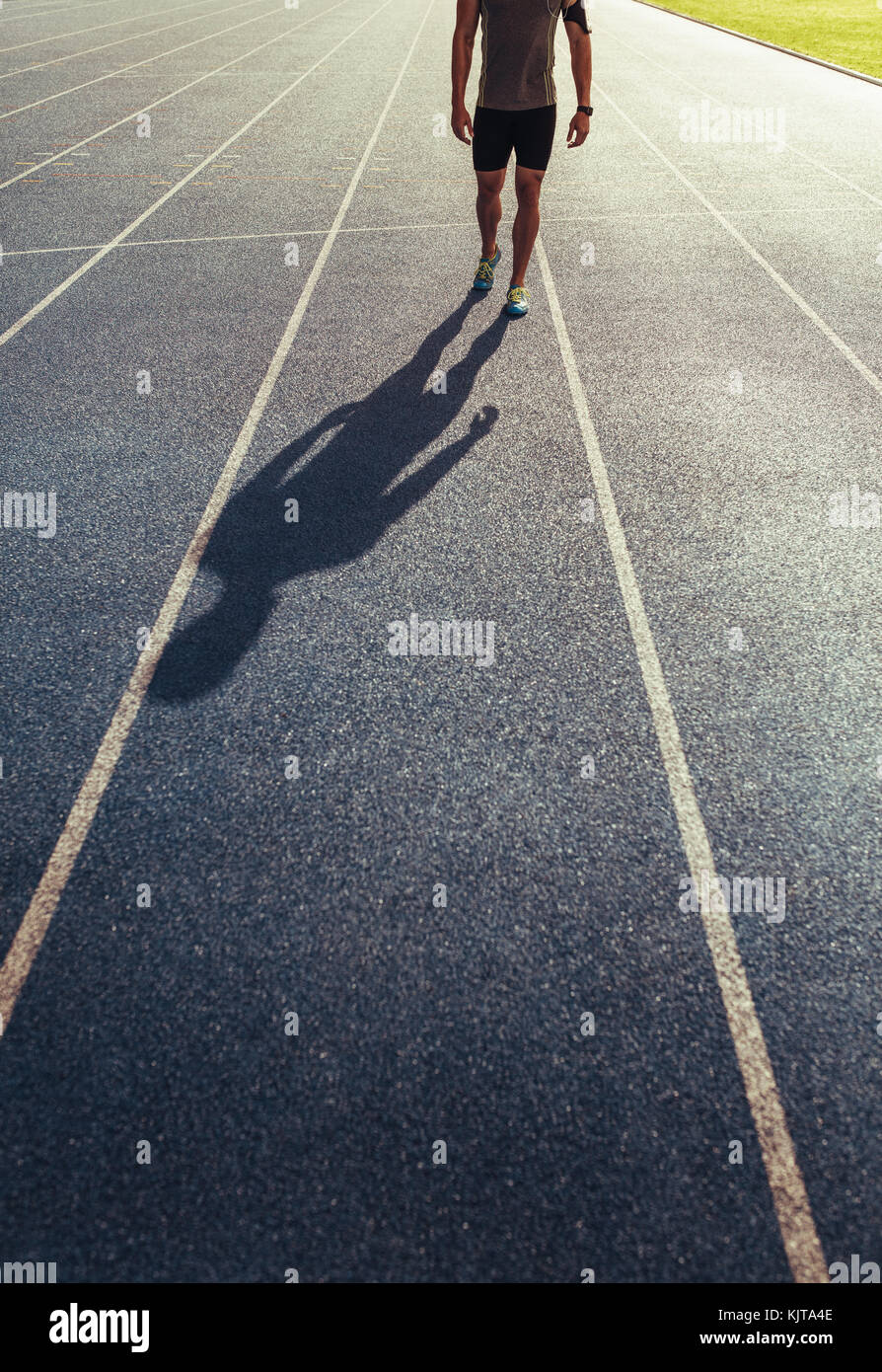 Atleta che cammina su un all-weather in esecuzione via l'ascolto di musica. Ombra di un runner di camminare sulla via. Foto Stock