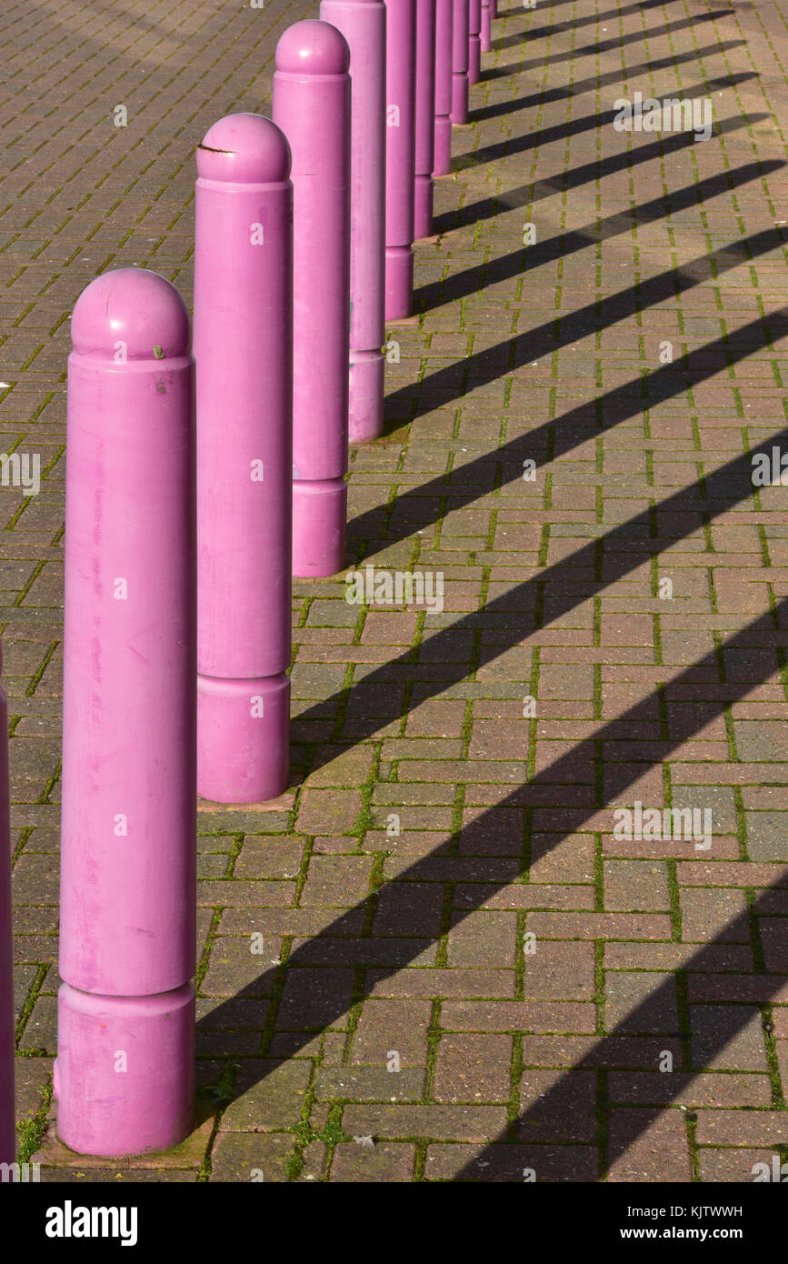 Una fila di vivacemente colorato di rosa parcheggio in plastica paracarri colata shaddows lunga sul blocco di pavimentazione al pomeriggio di sole. parcheggio coni di controllo. Foto Stock