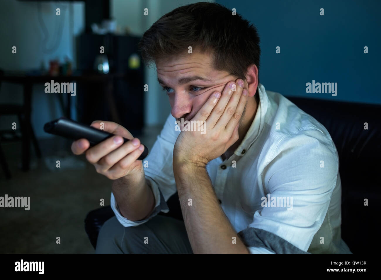 Annoiato uomo caucasico guardando la tv e lo zapping seduto su un divano a casa o in albergo. Foto Stock