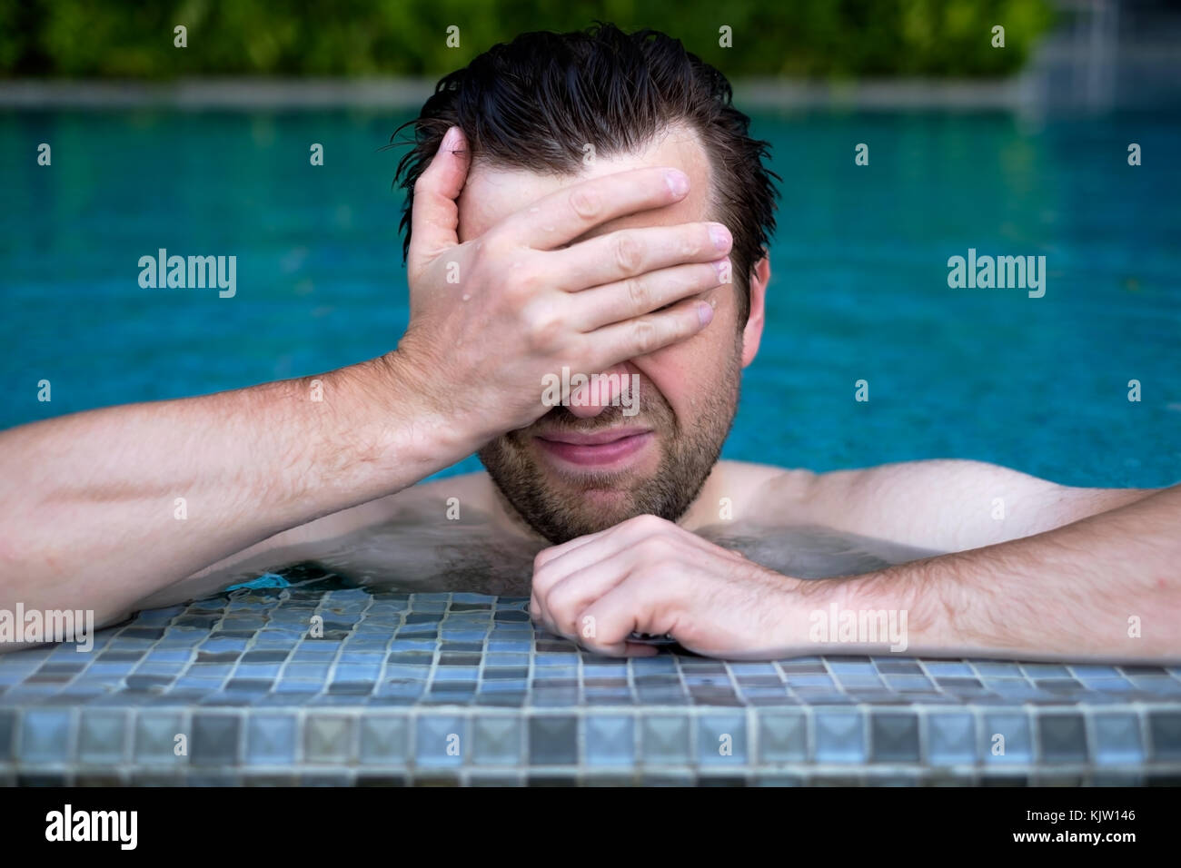 Un giovane uomo nel pool delle salviette viso con la sua mano. Foto Stock