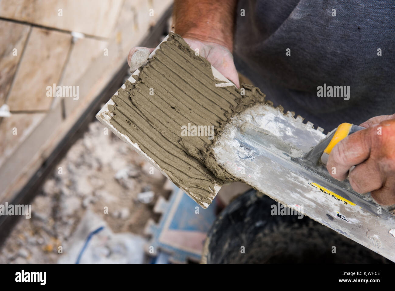 Malta essendo applicato ad una piastrella con una cazzuola scanalato per aderire alla superficie di montaggio. Foto Stock