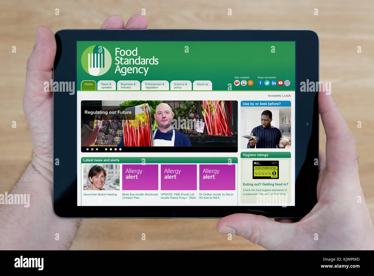 Un uomo guarda la Food Standards Agency del sito web sul suo iPad dispositivo tablet, sparato contro un tavolo di legno top sfondo (solo uso editoriale) Foto Stock