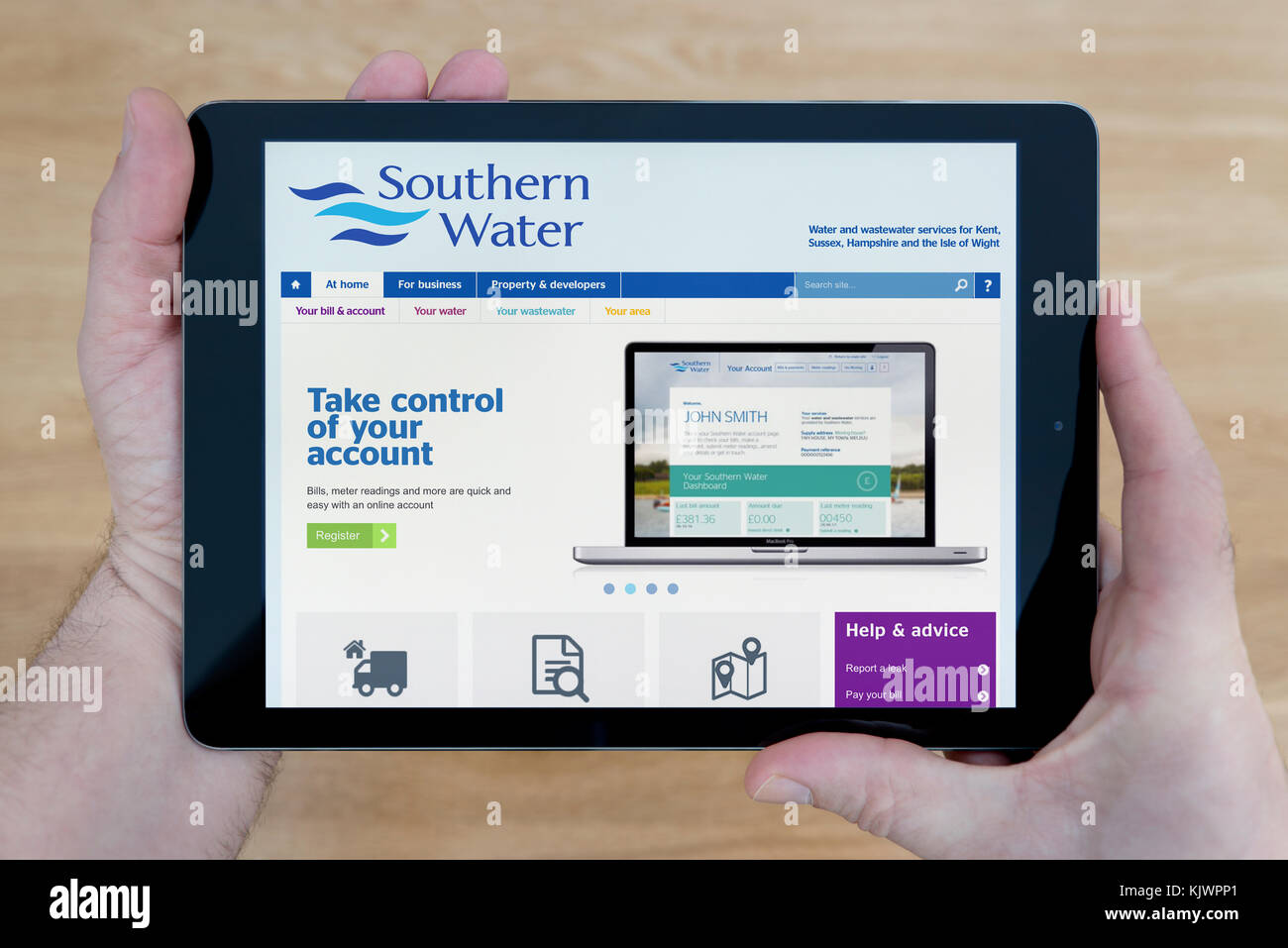 Un uomo guarda a sud del sito web di acqua sul suo iPad dispositivo tablet, sparato contro un tavolo di legno top sfondo (solo uso editoriale) Foto Stock