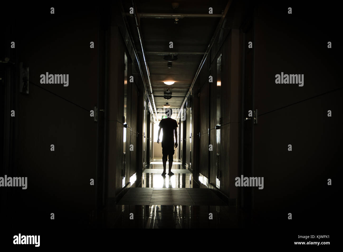 Uomo che cammina verso il basso un lungo corridoio scuro Foto Stock