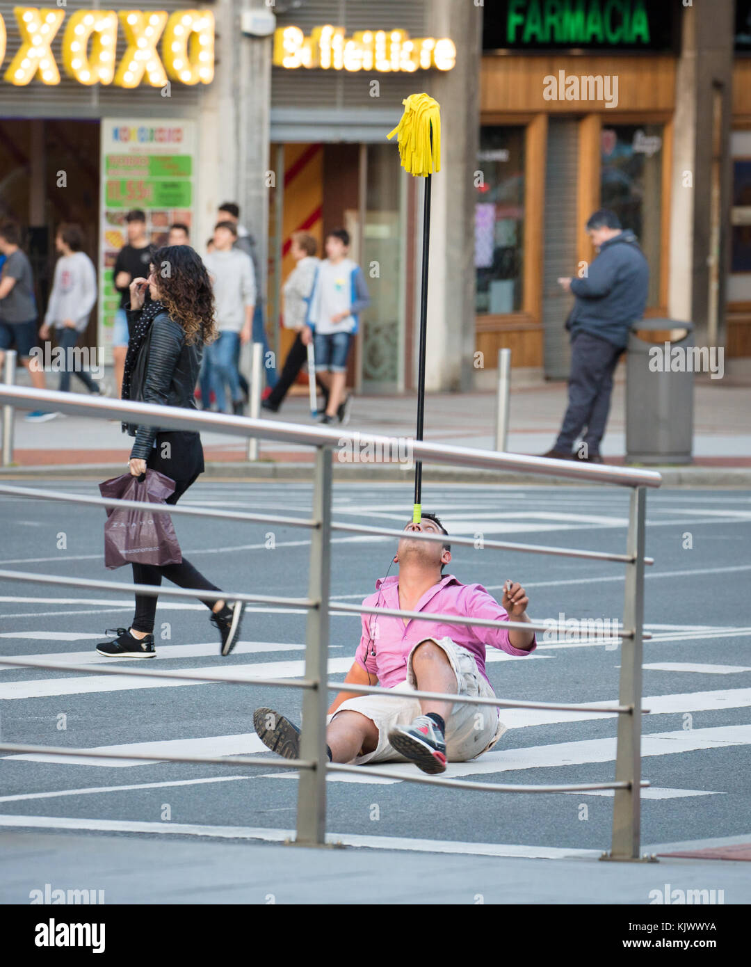 Un esecutore di strada seduti su un attraversamento pedonale a Bilbao Spagna settentrionale equilibratura di un pavimento mop sul suo naso mentre fumando una sigaretta Foto Stock