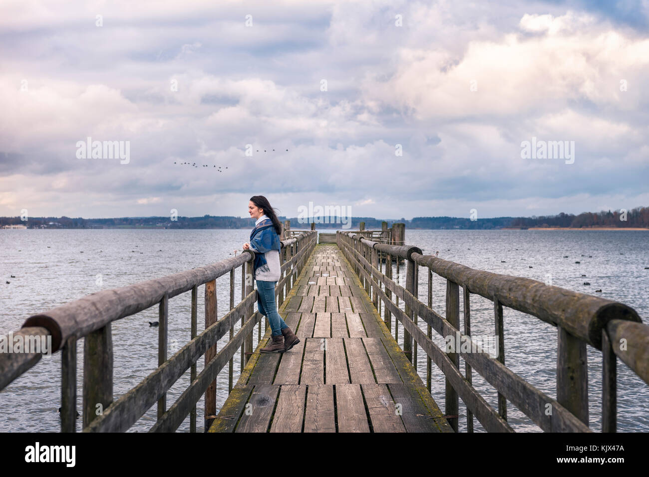 Destinazione romantica immagine a tema con una donna seduta da sola su un ponte rustico, sopra il famoso lago di Chiemsee in Baviera, Germania Foto Stock
