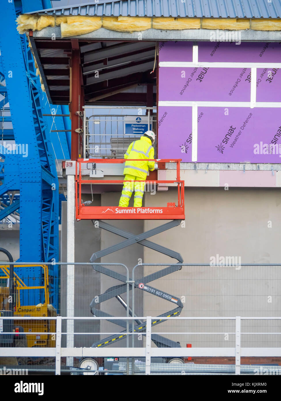 Workman su una forbice di tipo man paranco isolato di fissaggio dei pannelli di rivestimento sull'esterno di un piccolo edificio industriale Foto Stock