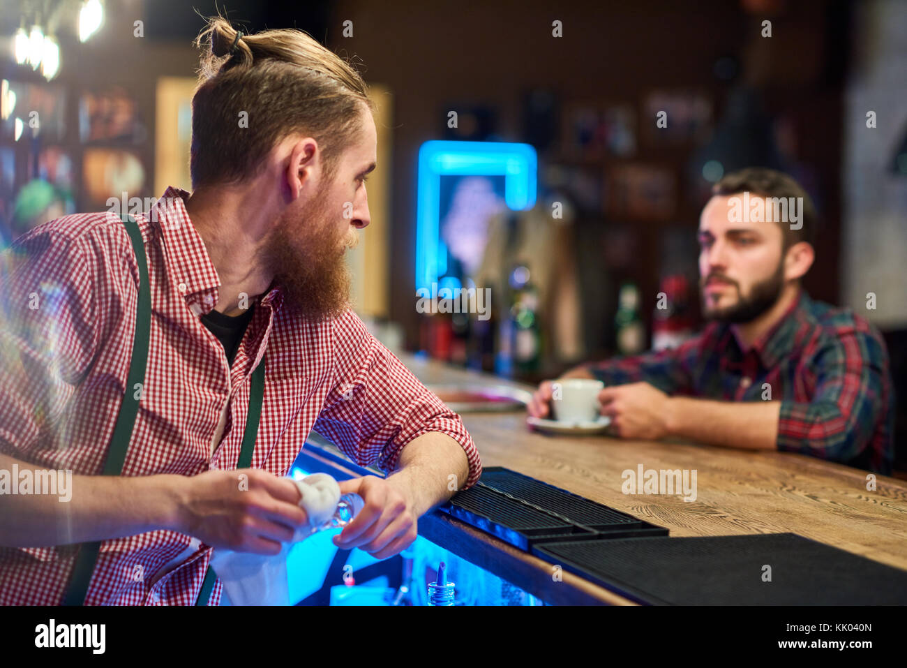 Ritratto di moderna barista barbuto di parlare al cliente al bancone bar in pub, messa a fuoco sul primo piano, spazio di copia Foto Stock