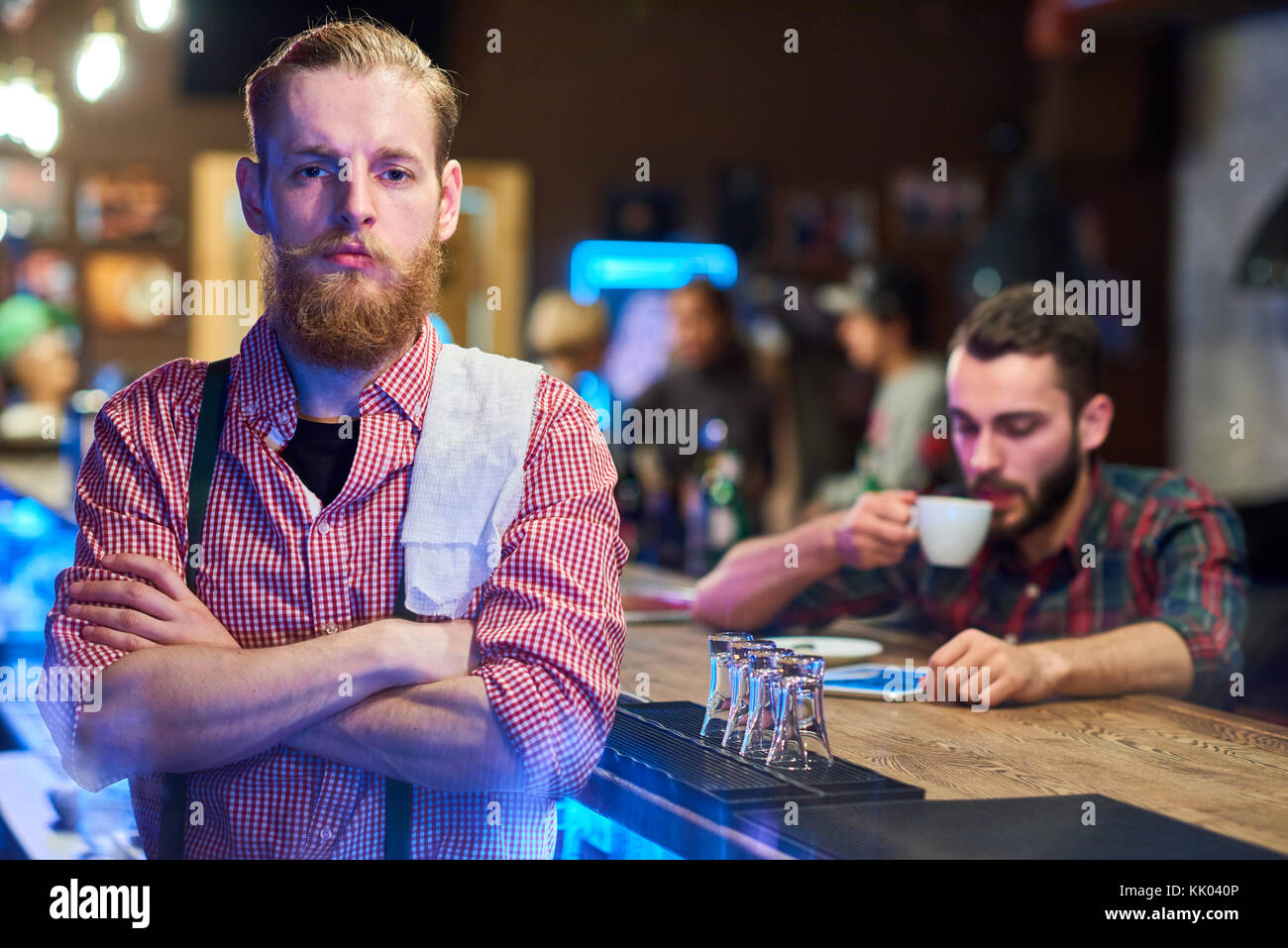 Ritratto di bello barbuto barista in posa con le braccia incrociate guardando con fiducia alla fotocamera in piedi dietro il bancone bar in pub, spazio di copia Foto Stock