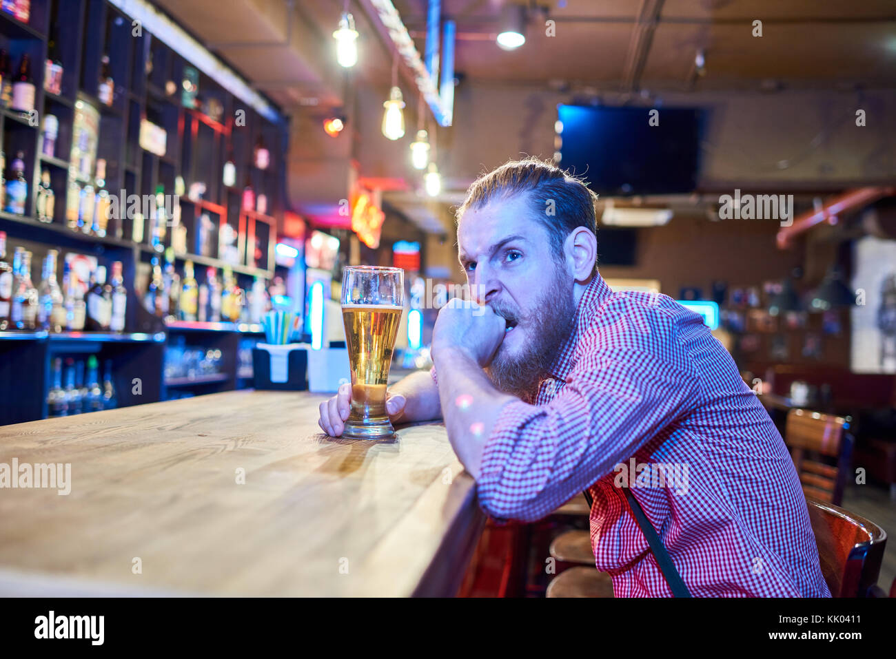 Ritratto di ansioso uomo barbuto guardando preoccupata e arrabbiato mentre si guarda la partita di sport in TV seduti al bancone bar in pub con bicchiere di birra, cop Foto Stock