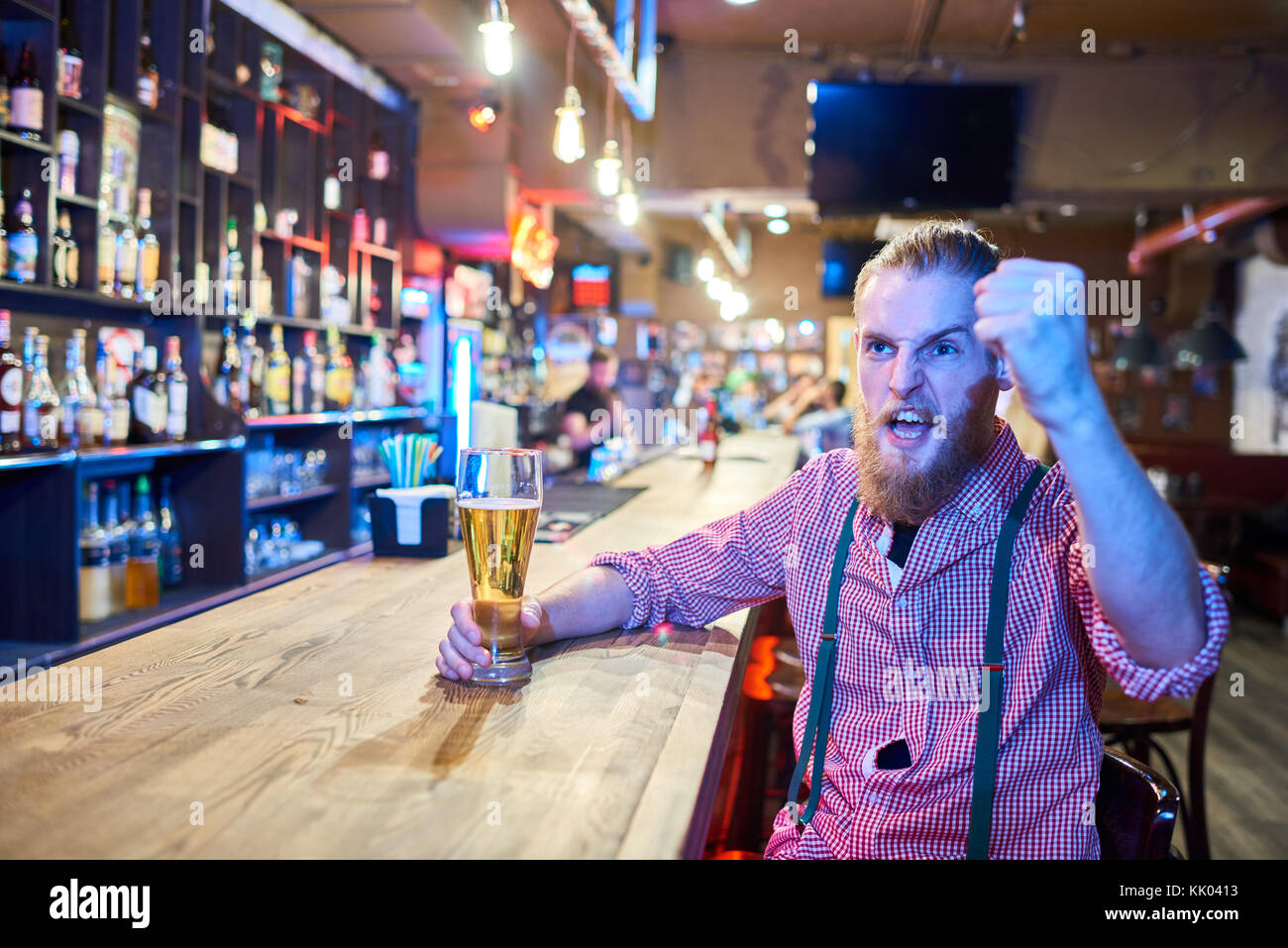 Ritratto di emozionale uomo barbuto tifo mentre si guarda la partita di sport in TV seduti al bancone bar in pub con bicchiere di birra, spazio di copia Foto Stock