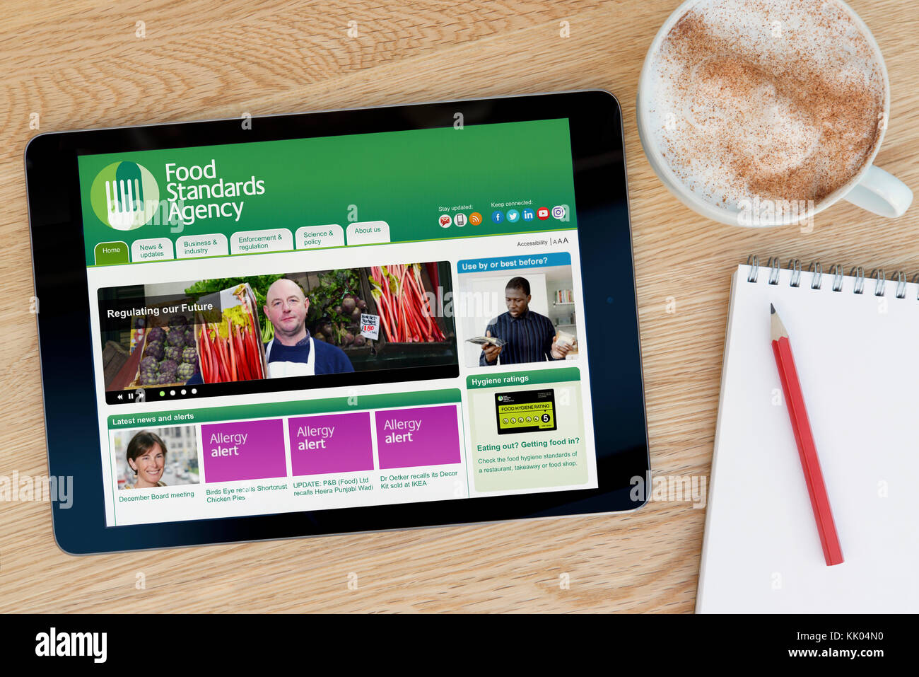 Un uomo guarda la Food Standards Agency del sito web sul suo iPad dispositivo tablet, sparato contro un tavolo di legno top sfondo (solo uso editoriale) Foto Stock