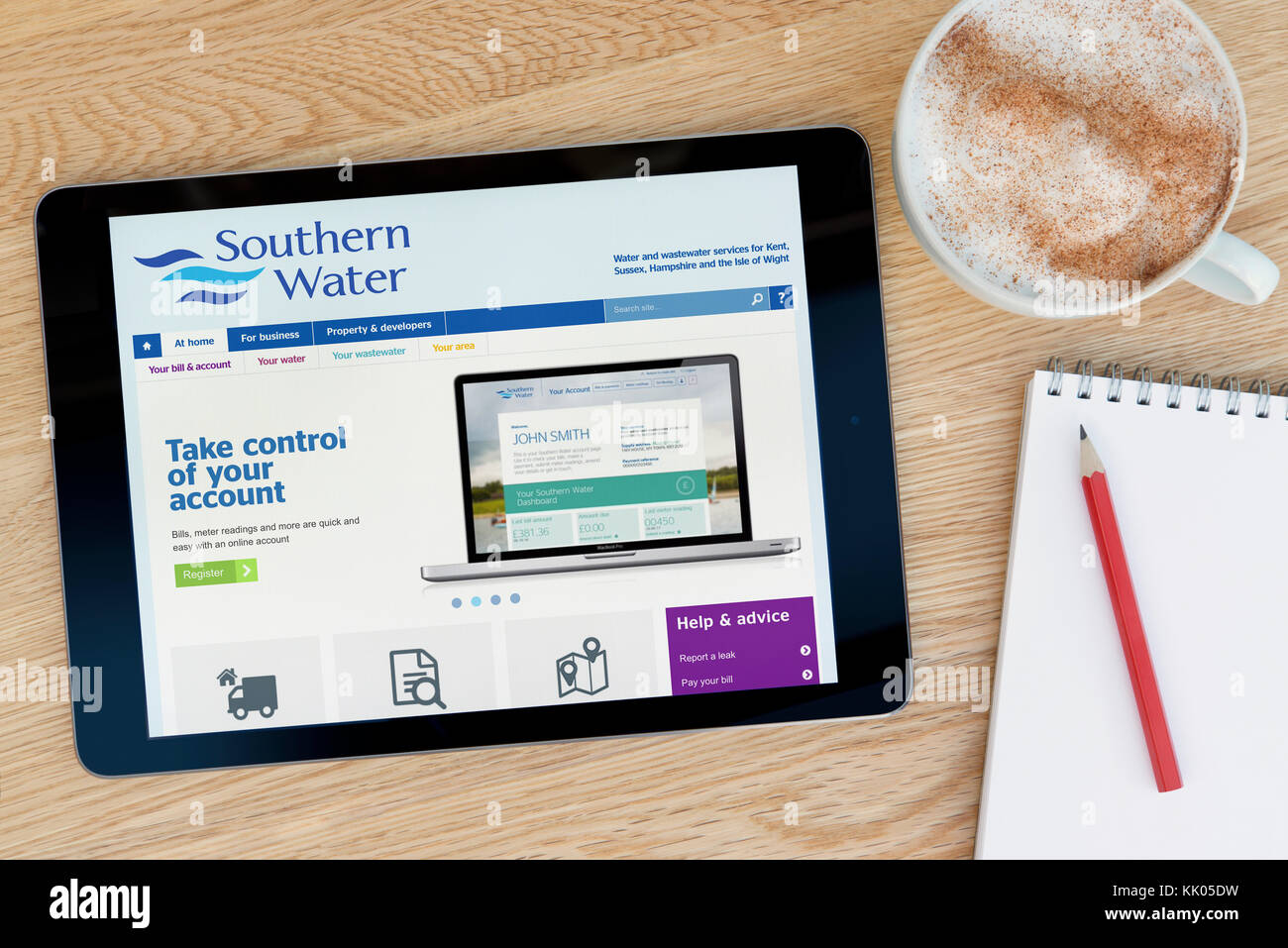 Un uomo guarda a sud del sito web di acqua sul suo iPad dispositivo tablet, sparato contro un tavolo di legno top sfondo (solo uso editoriale) Foto Stock