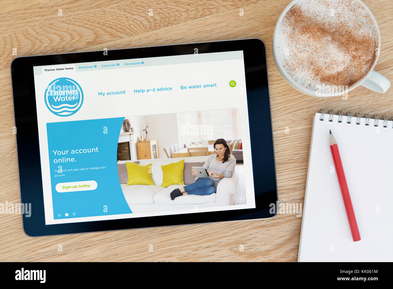 Un uomo guarda la Thames Water sito sul suo iPad dispositivo tablet, sparato contro un tavolo di legno top sfondo (solo uso editoriale) Foto Stock