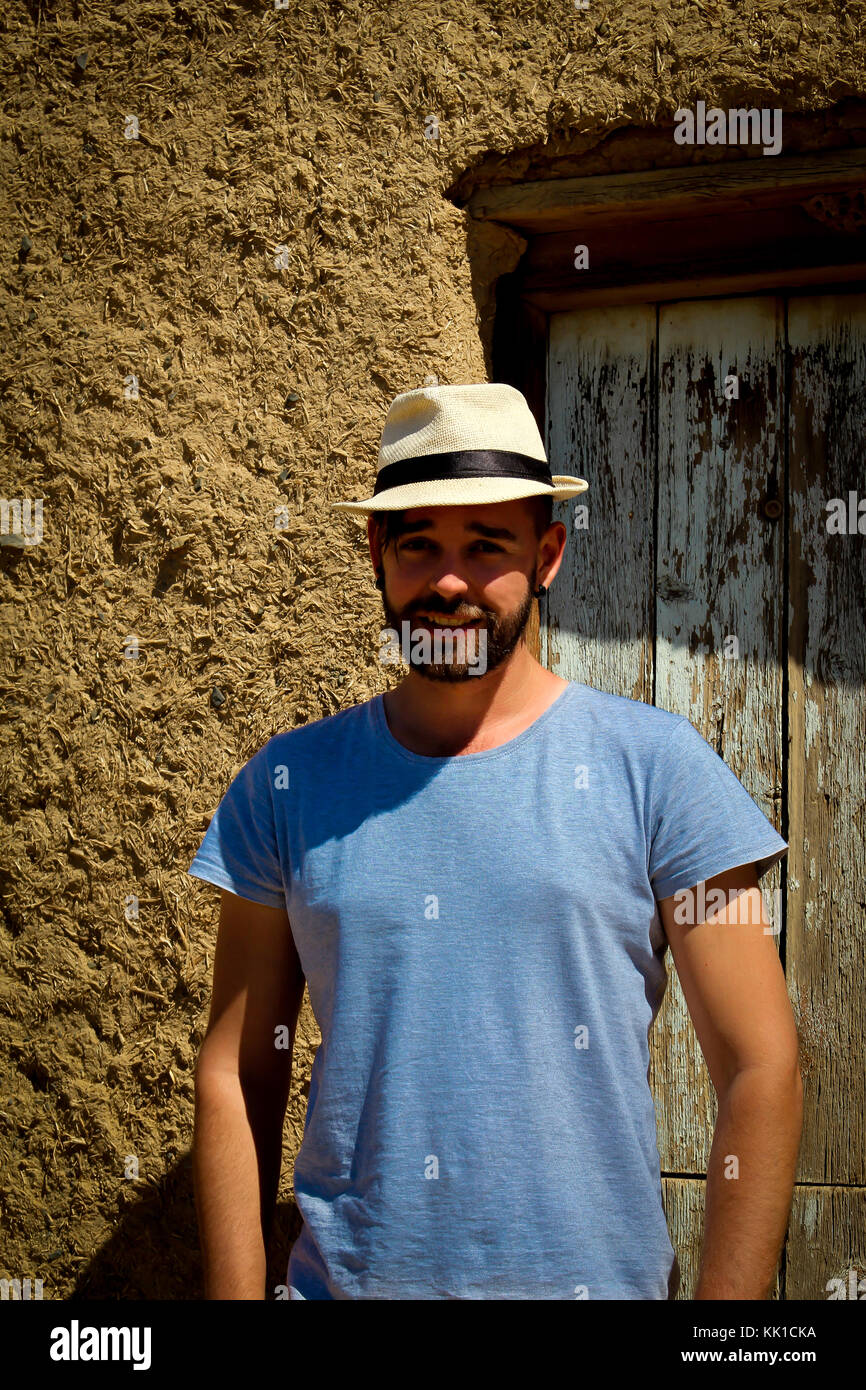 Uomo caucasico sorridente con hat su in piedi nella parte anteriore della porta della casa di fango Foto Stock