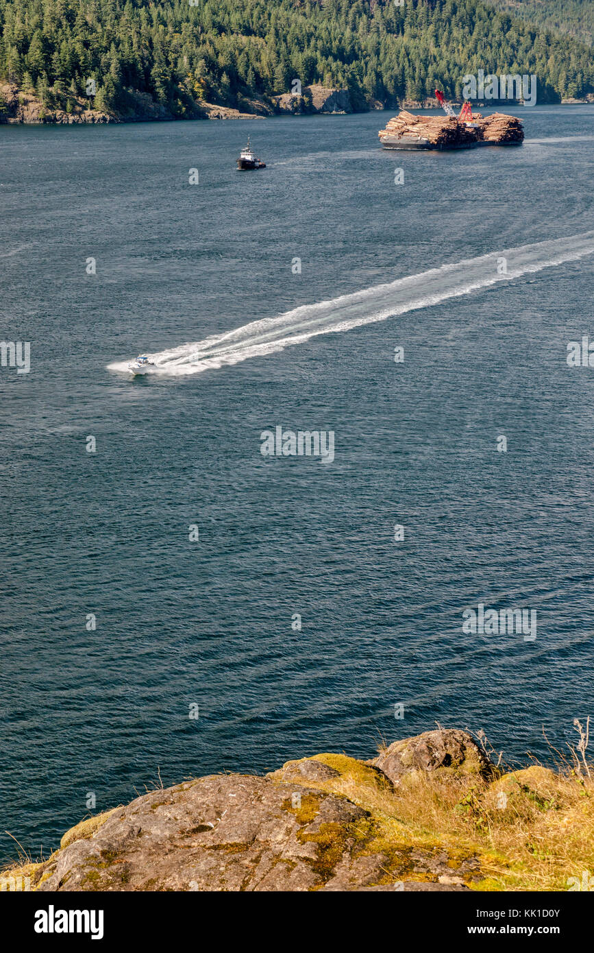 Speeedboat passando ITB Beaufort Sea, non proiettato barge, caricato con il legname, in Seymour si restringe alla scoperta passaggio dall isola Maude, BC, Canada Foto Stock