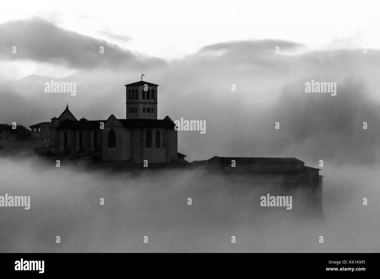 Bella vista di San Francesco Chiesa (Assisi) all'alba, sopra un mare di nebbia Foto Stock