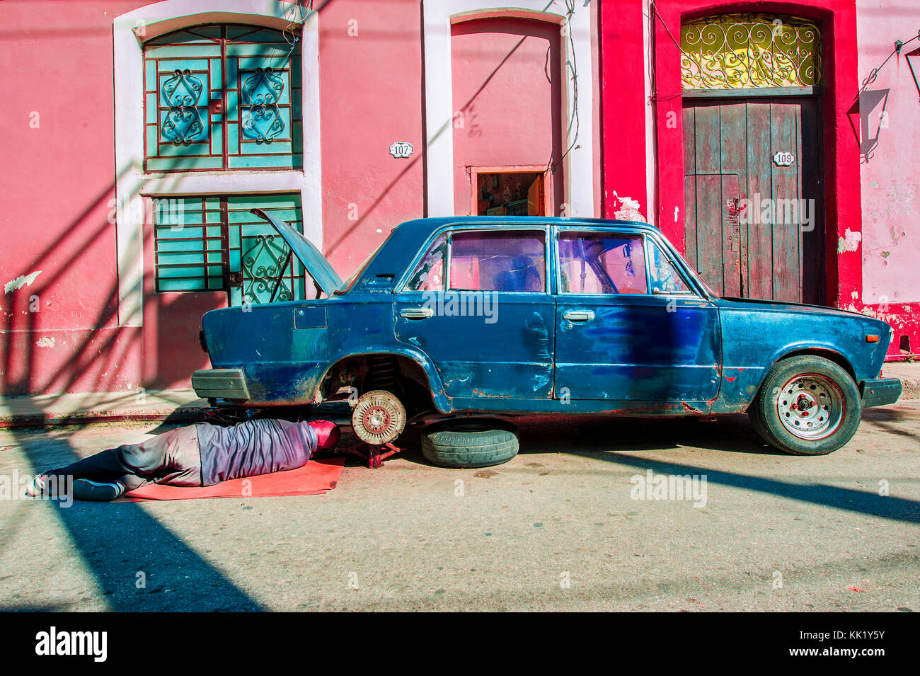 Un uomo che ripara la sua vecchia auto di fronte alla sua casa al Centro dell'Avana, Cuba Foto Stock