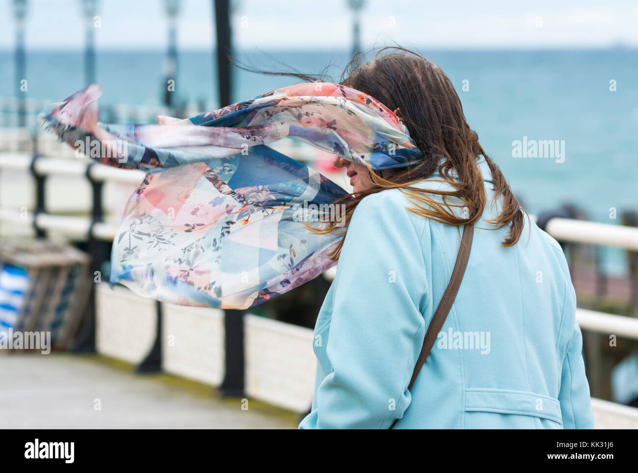 Donna che cammina in una giornata di vento in autunno con un cappotto e sciarpa al vento, nel Regno Unito. Foto Stock