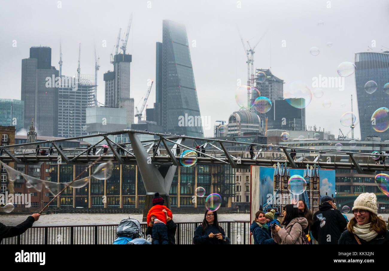 Banca del sud del fiume Tamigi uomo percorso di intrattenimento per bambini e persone che fanno grandi bolle, Londra, Inghilterra, Regno Unito con il Millennium Bridge, grattacieli della città Foto Stock