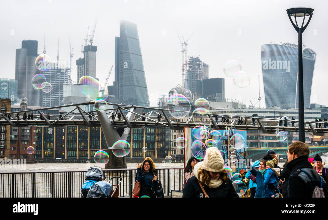 Banca del sud del fiume Tamigi uomo percorso di intrattenimento per bambini e persone che fanno grandi bolle, Londra, Inghilterra, Regno Unito con il Millennium Bridge, grattacieli della città Foto Stock