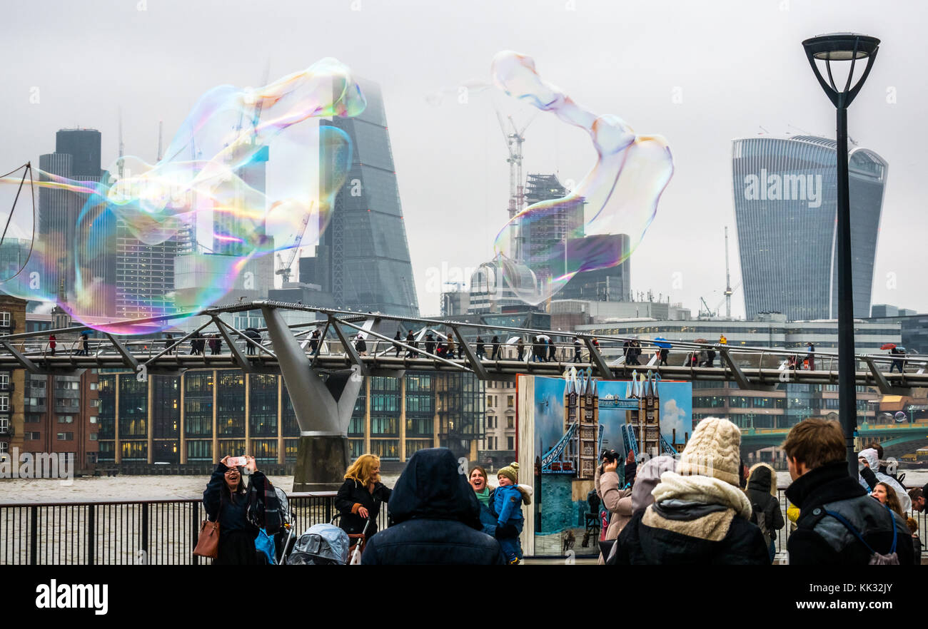 Banca del sud del fiume Tamigi uomo percorso di intrattenimento per bambini e persone che fanno grandi bolle, Londra, Inghilterra, Regno Unito con il Millennium Bridge, grattacieli della città Foto Stock