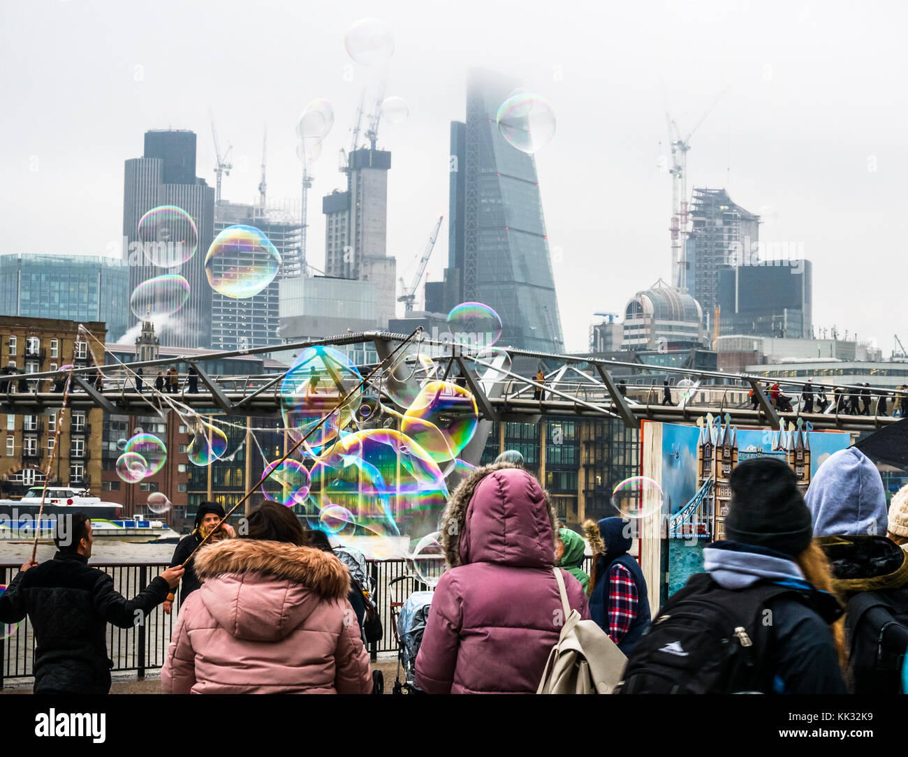 Banca del sud del fiume Tamigi uomo percorso di intrattenimento per bambini e persone che fanno grandi bolle, Londra, Inghilterra, Regno Unito con il Millennium Bridge, grattacieli della città Foto Stock